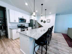 Kitchen featuring pendant lighting, white cabinets, appliances with stainless steel finishes, a kitchen island, and a kitchen bar