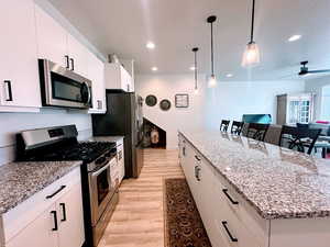 Kitchen featuring white cabinetry, hanging light fixtures, stainless steel appliances, and a kitchen island