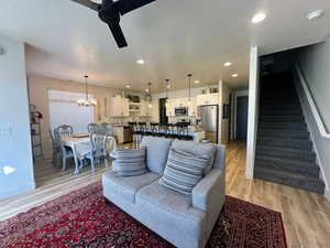 Living room featuring a textured ceiling, ceiling fan with notable chandelier, and light hardwood / wood-style flooring