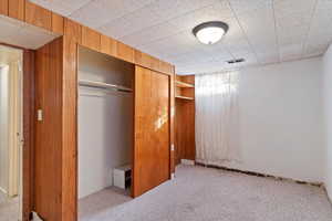 Unfurnished bedroom with wood walls, light colored carpet, and a closet