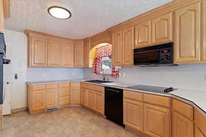 Kitchen with sink, light brown cabinets, black appliances, and a textured ceiling