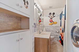 Bathroom with toilet, washer / dryer, a textured ceiling, tile walls, and vanity