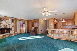 Unfurnished living room featuring wooden walls, dark carpet, a textured ceiling, and a stone fireplace