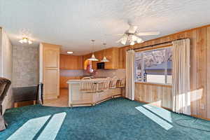 Kitchen featuring light brown cabinetry, a textured ceiling, decorative light fixtures, light colored carpet, and kitchen peninsula