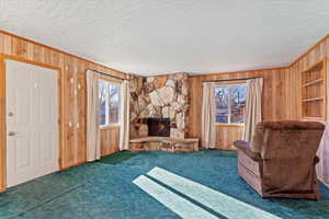 Unfurnished living room with a fireplace, wood walls, a textured ceiling, and dark carpet