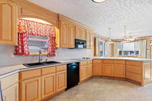 Kitchen featuring black appliances, light brown cabinetry, hanging light fixtures, sink, and kitchen peninsula