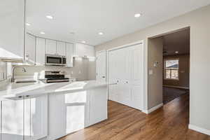 Kitchen featuring white cabinets, appliances with stainless steel finishes, sink, kitchen peninsula, and hardwood / wood-style flooring