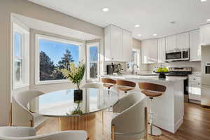 Kitchen featuring light wood-type flooring, stainless steel appliances, white cabinetry, and a kitchen bar