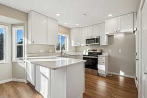 Kitchen with light hardwood / wood-style floors, appliances with stainless steel finishes, white cabinets, sink, and kitchen bar