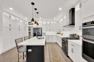 Kitchen with a kitchen bar, appliances with stainless steel finishes, white cabinetry, an island with sink, and wall chimney exhaust hood