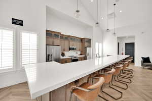 Kitchen with high vaulted ceiling, decorative light fixtures, appliances with stainless steel finishes, and a spacious island