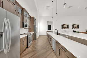 Kitchen featuring pendant lighting, appliances with stainless steel finishes, a towering ceiling, decorative backsplash, and sink