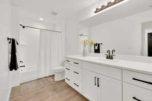 Full bathroom featuring hardwood / wood-style floors, toilet, shower / bath combination with curtain, and vanity