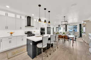 Kitchen featuring stainless steel stove, white cabinets, sink, an island with sink, and wall chimney exhaust hood