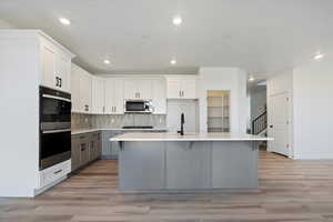 Kitchen featuring white cabinetry, stainless steel appliances, sink, and a center island with sink