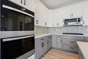 Kitchen with white cabinetry, gray cabinets, tasteful backsplash, and appliances with stainless steel finishes