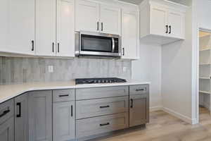 Kitchen with gray cabinets, light hardwood / wood-style flooring, stainless steel appliances, tasteful backsplash, and white cabinets