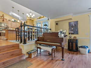 Misc room with light hardwood / wood-style flooring, crown molding, a notable chandelier, and vaulted ceiling