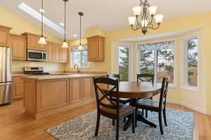 Dining space with recessed lighting, light wood-type flooring, vaulted ceiling with skylight, and a notable chandelier