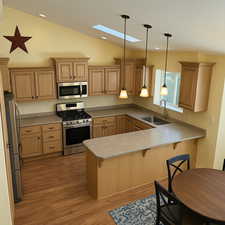 Kitchen with a sink, a peninsula, stainless steel appliances, a kitchen bar, and lofted ceiling with skylight