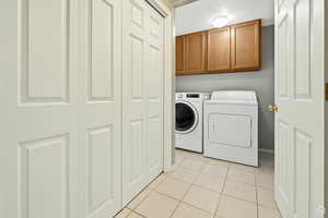 Washroom with light tile patterned floors, cabinet space, and washer and clothes dryer