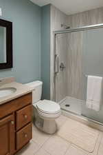 Bathroom with a stall shower, tile patterned flooring, toilet, and vanity