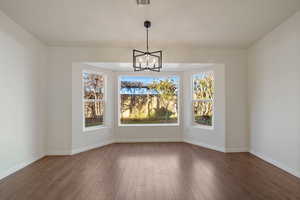 Unfurnished dining area featuring dark hardwood / wood-style flooring and a notable chandelier