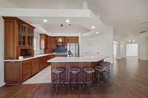 Kitchen with a spacious island, custom exhaust hood, stainless steel refrigerator with ice dispenser, decorative columns, and a breakfast bar