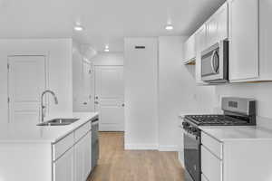 Kitchen with sink, white cabinets, light wood-type flooring, and appliances with stainless steel finishes