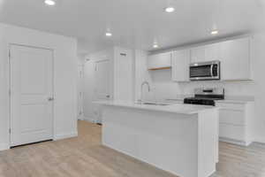 Kitchen with light hardwood / wood-style floors, appliances with stainless steel finishes, a kitchen island with sink, sink, and white cabinets