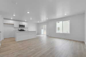 Kitchen featuring appliances with stainless steel finishes, sink, white cabinets, a center island with sink, and light hardwood / wood-style floors