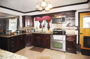 Kitchen with a chandelier, light tile patterned floors, sink, ornamental molding, and stainless steel appliances