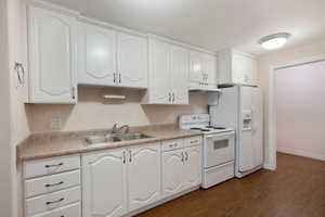 Kitchen with dark wood-type flooring, sink, white appliances, and white cabinets