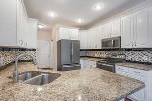 Kitchen with decorative backsplash, appliances with stainless steel finishes, sink, and white cabinetry