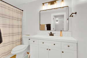 Bathroom with a shower with curtain, toilet, tasteful backsplash, and vanity