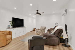 Living room with ceiling fan, light hardwood / wood-style floors, and a wall unit AC