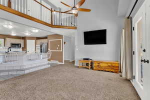 Unfurnished living room featuring ceiling fan, sink, a towering ceiling, and carpet flooring