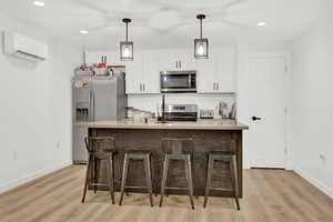 Kitchen with stainless steel appliances, white cabinetry, a center island with sink, and a wall mounted air conditioner