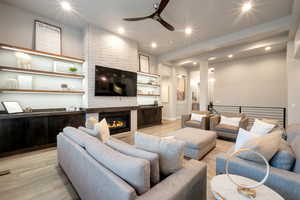 Living room with ceiling fan, a large fireplace, and light hardwood / wood-style flooring