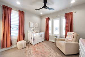 Carpeted bedroom with ceiling fan and a nursery area