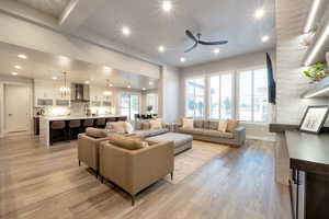 Living room featuring light wood-type flooring, ceiling fan with notable chandelier, and a healthy amount of sunlight