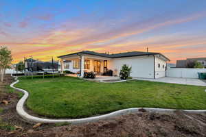 Back house at dusk featuring a patio, a trampoline, and a lawn