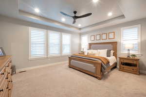 Carpeted bedroom featuring ceiling fan, multiple windows, and a tray ceiling