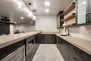 Kitchen with beverage cooler, decorative light fixtures, sink, backsplash, and stainless steel microwave