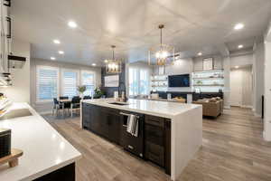 Kitchen featuring hanging light fixtures, sink, light wood-type flooring, white cabinetry, and an island with sink