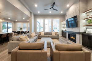 Living room featuring ceiling fan, a stone fireplace, and light hardwood / wood-style flooring