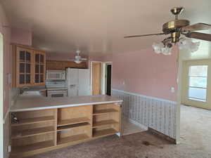 Kitchen with sink, white appliances, kitchen peninsula, and light colored carpet