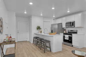 Kitchen featuring light hardwood / wood-style floors, appliances with stainless steel finishes, white cabinetry, a kitchen breakfast bar, and kitchen peninsula