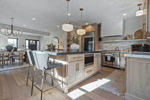 Kitchen featuring a center island, appliances with stainless steel finishes, decorative light fixtures, wall chimney exhaust hood, and light brown cabinets