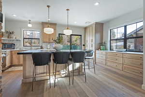 Kitchen with decorative light fixtures, light hardwood / wood-style flooring, light brown cabinetry, and decorative backsplash